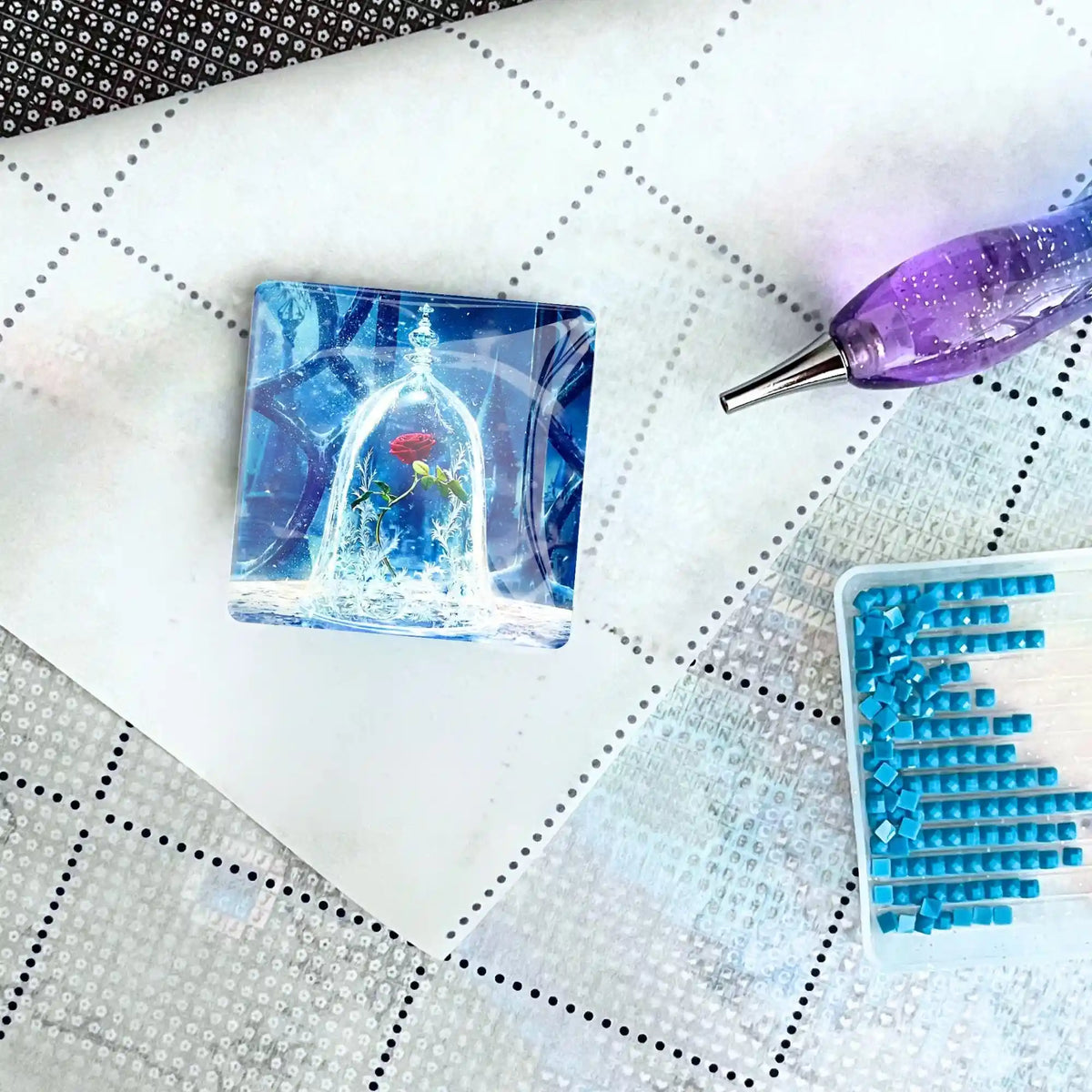 Quadratischer Rose im Wunderglas Cover Minder auf einer Diamond Painting Leinwand mit Stift und blauen Diamanten.
