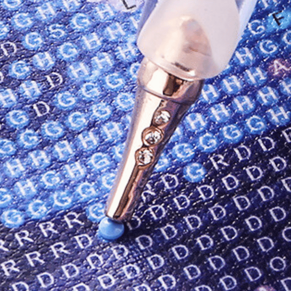 Ergonomischer Diamond Painting Stift Rosé & Diamant beim Platzieren eines blauen Steinchens auf der Leinwand