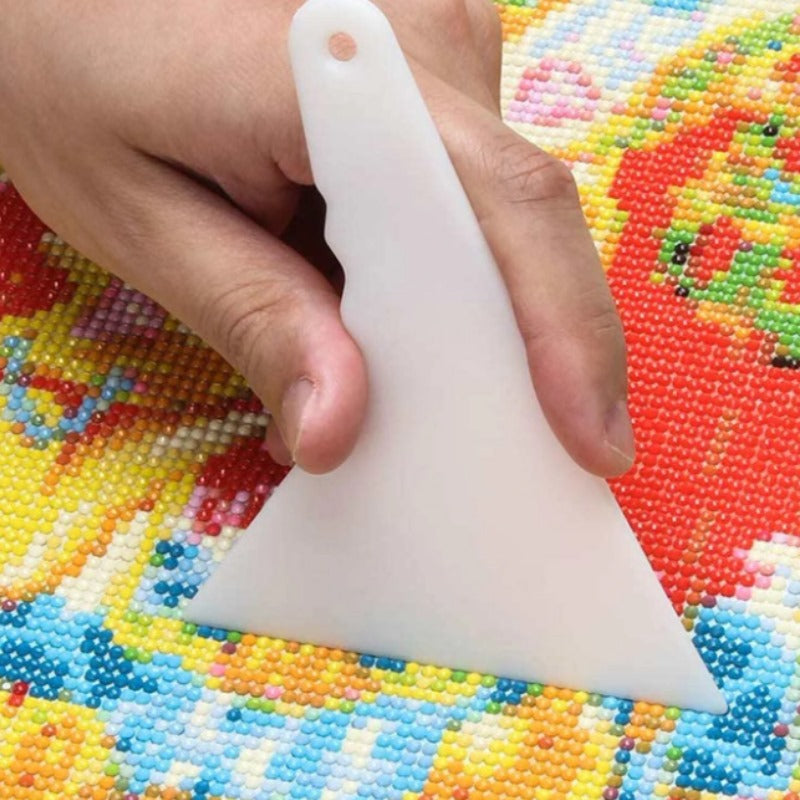 Weißer Korrekturschieber zum Ausrichten von Steinen bei einem bunten Diamond Painting auf buntem Mosaik