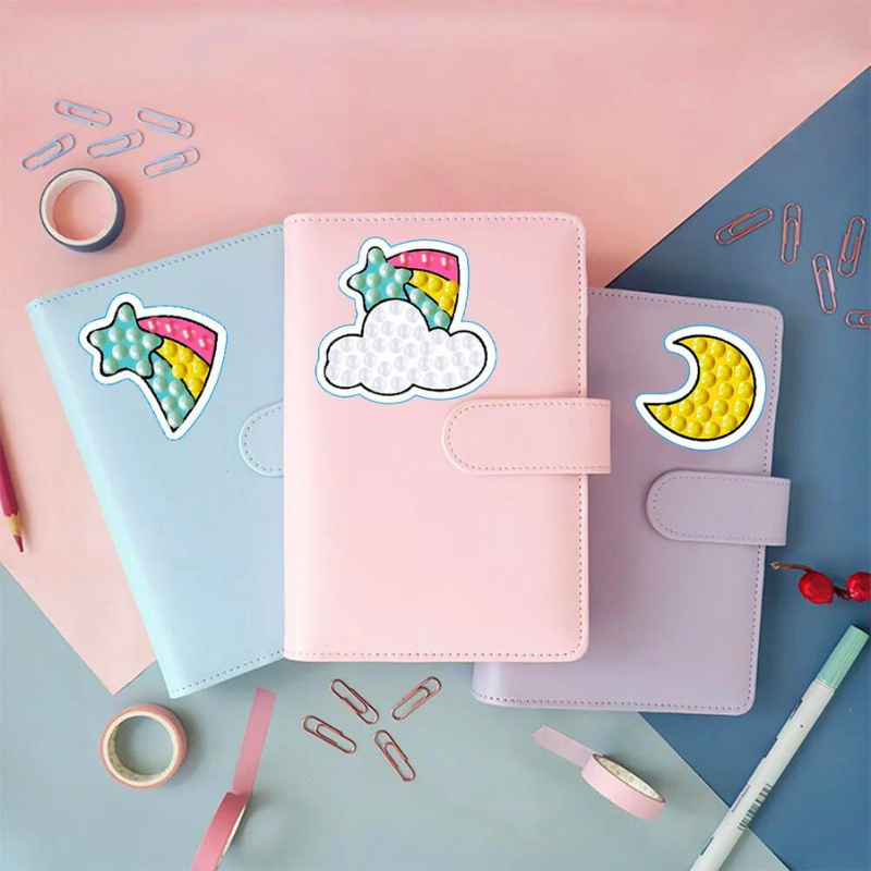 Bunte Diamond Painting Sticker mit Einhorn-Motiven, Sternen und Mond auf pastellfarbenen Notizbüchern zur Dekoration.