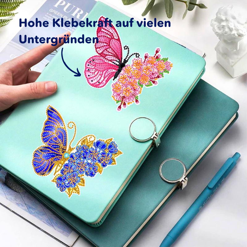 Glitzernde Diamond Painting Sticker mit bunten Schmetterlingen auf einem türkisfarbenen Notizbuch als DIY-Deko