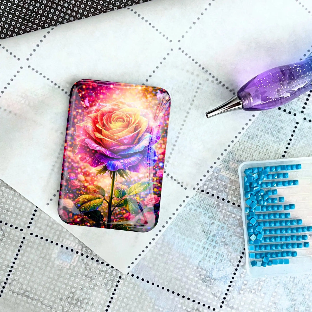 Diamond Painting Cover Minder aus Glas mit bunter Rose auf Leinwand neben Glitzer-Stift und Steinen