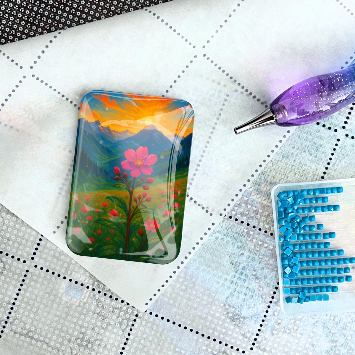 Glas Cover Minder für Diamond Painting mit Gebirgsblumen Motiv, platziert auf einer Leinwand mit Stift und Steinchen.