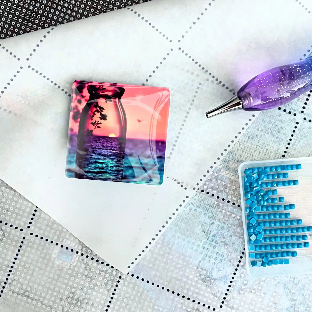 Quadratischer Cover Minder mit Sonnenuntergang-Motiv auf einer Diamond Painting Leinwand mit Stift und Steinchen.