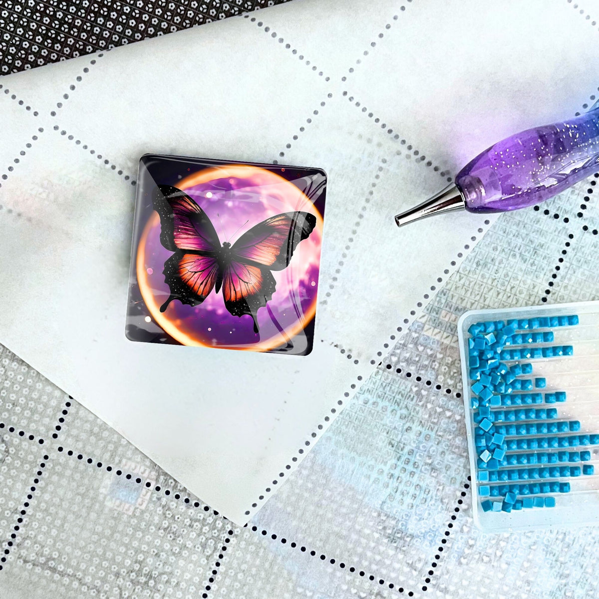 Lila Schmetterling Cover Minder aus Glas als magnetisches Zubehör für Diamond Painting auf einer Leinwand mit Stift.