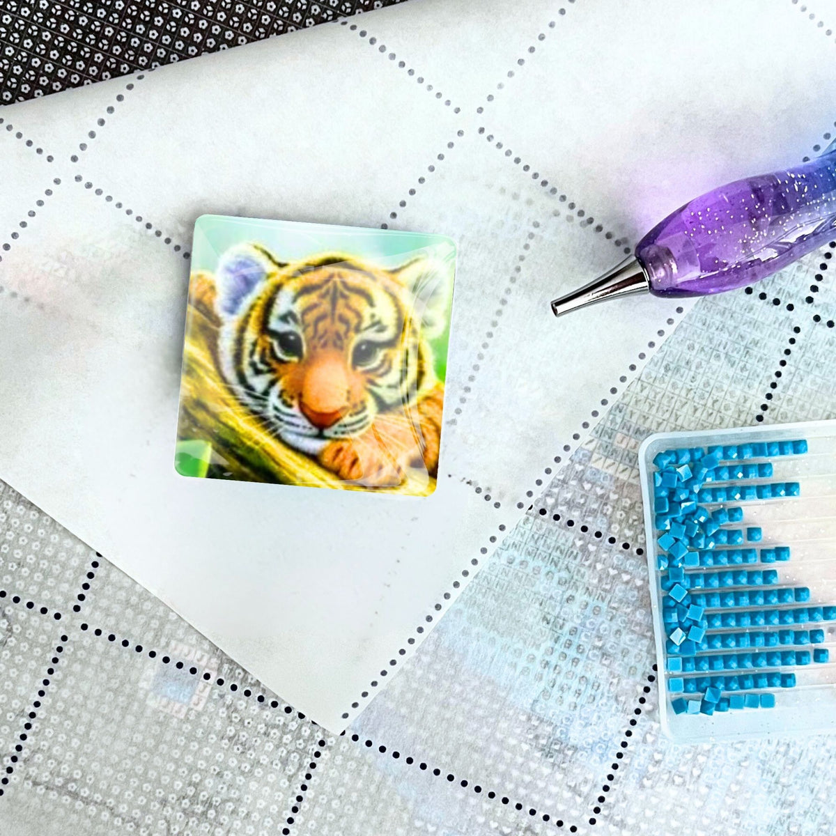 Tigerbaby Cover Minder aus Glas auf einer Diamond Painting Leinwand mit Stift und blauen Diamanten