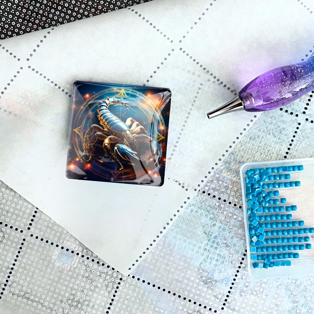 Diamond Painting Cover Minder mit Sternzeichen Skorpion Motiv auf einer Leinwand mit Stift und blauen Glitzersteinen