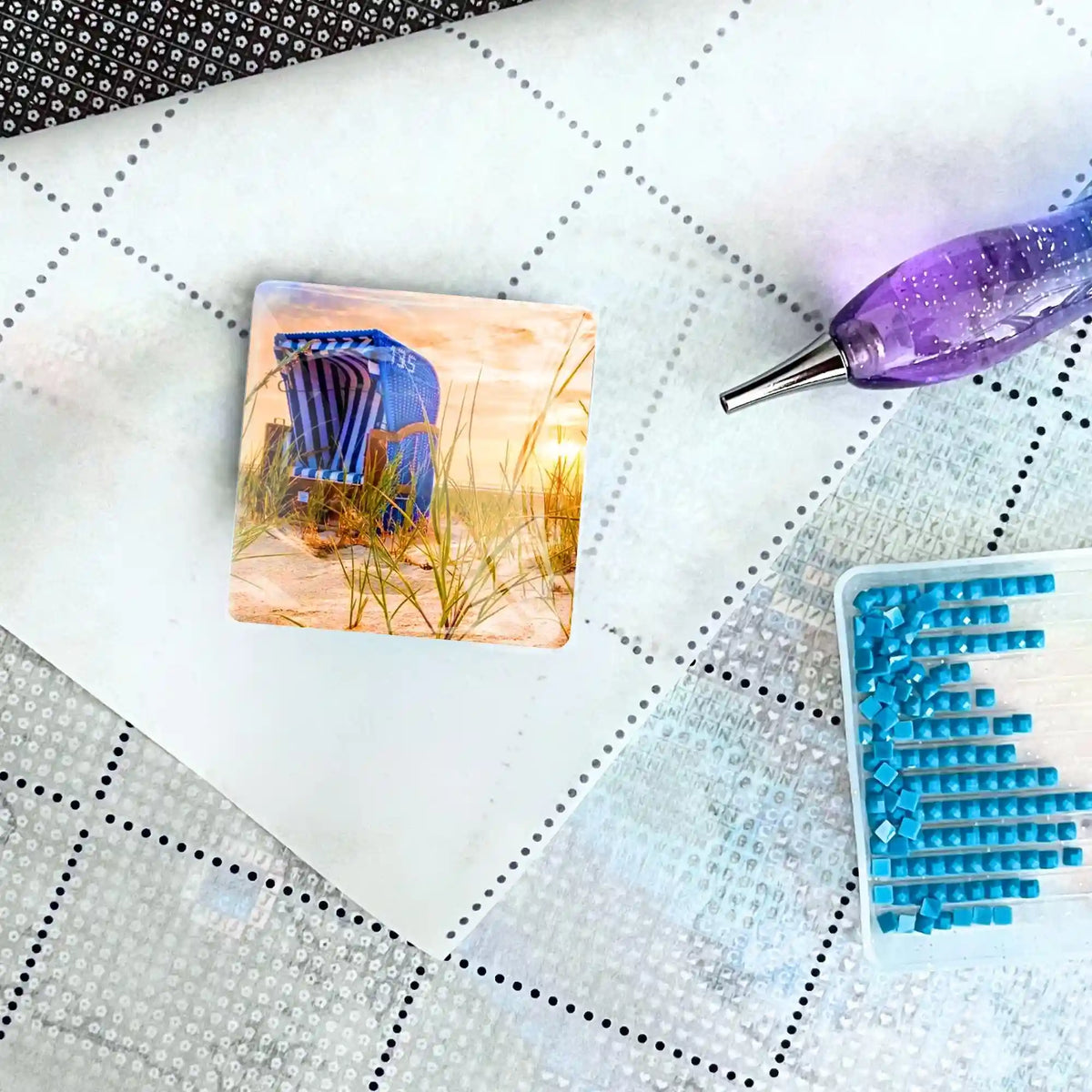 Glas Cover Minder mit Strandkorb-Motiv als Zubehör für dein Diamond Painting auf einer Leinwand mit Stift und Steinen.
