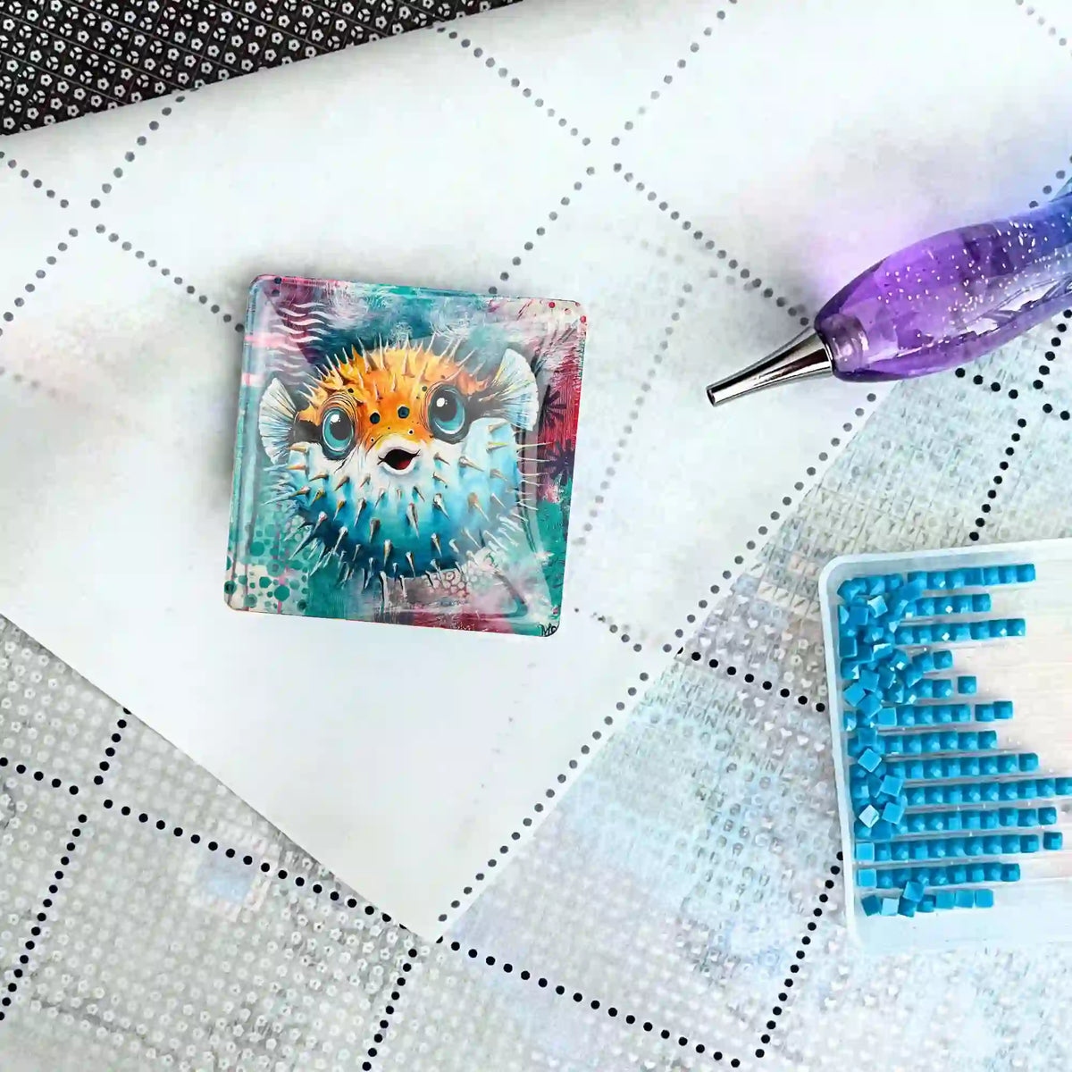 Quadratischer Kugelfisch-Coverminder aus Glas für Diamond Painting auf einer Leinwand mit Stift und blauen Diamanten.