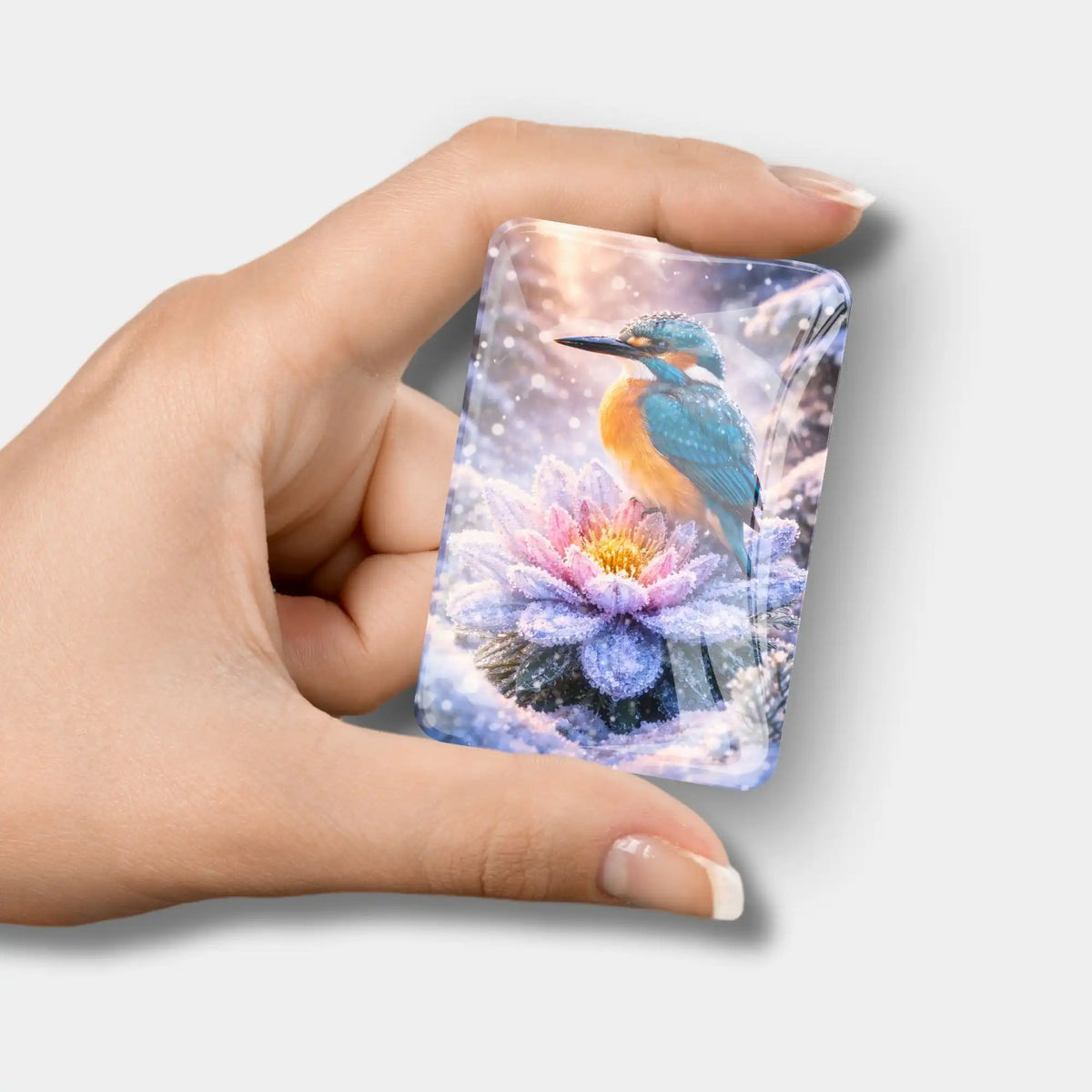 Diamond Painting Cover Minder aus Glas mit Eisvogel auf frostiger Seerose im Schnee, gehalten in der Hand.