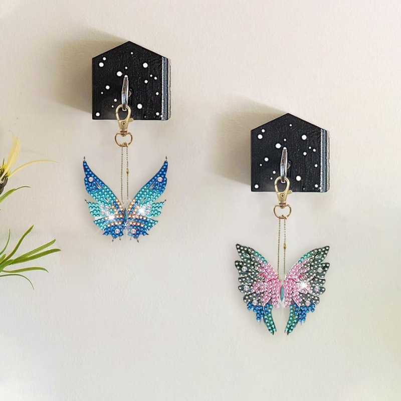 Zwei glitzernde Diamond Painting Schlüsselanhänger als Engelsflügel mit funkelnden Steinen an einer Wandhalterung