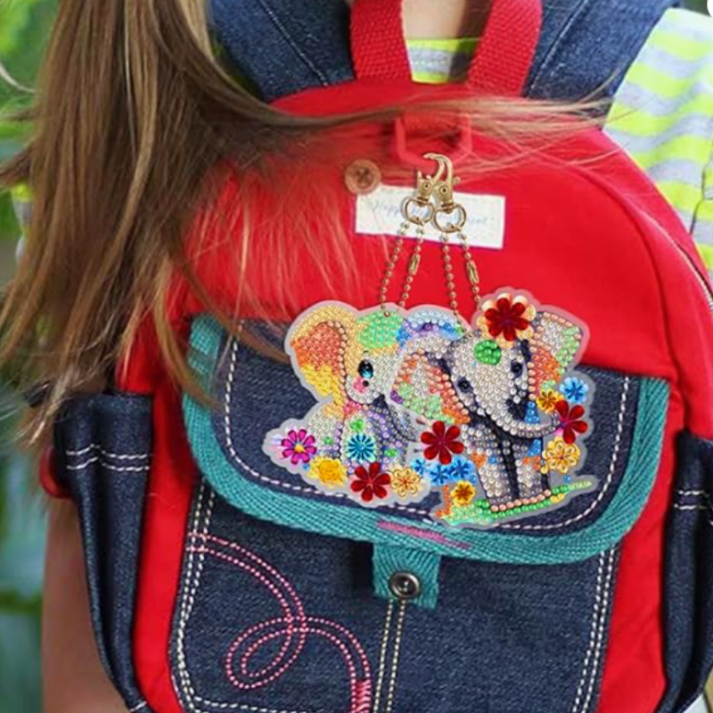 Glitzernde Diamond Painting Schlüsselanhänger mit süßen Elefanten-Motiven an einem bunten Kinder-Rucksack befestigt.