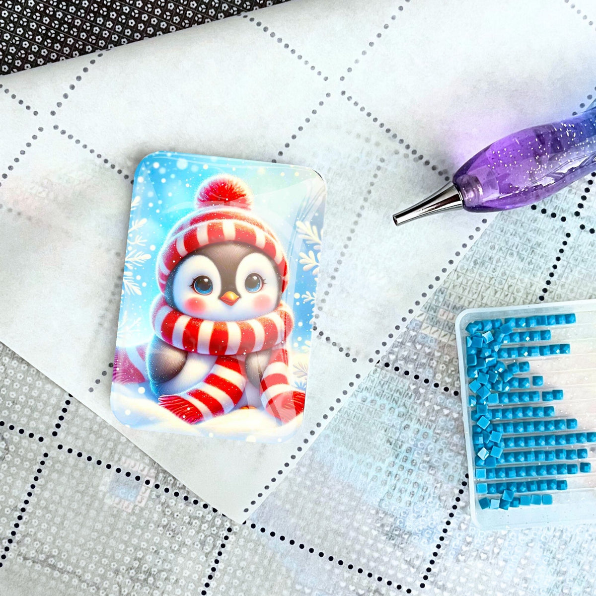 Pinguin Cover Minder aus Glas als magnetischer Halter für Diamond Painting auf einer Leinwand mit Stift und Steinchen.