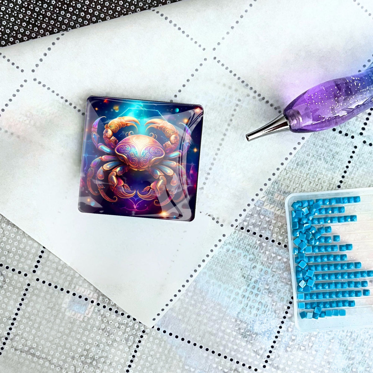 Diamond Painting Cover Minder mit Krebs Sternzeichen Motiv auf einer Leinwand mit Stift und blauen Diamant-Steinchen