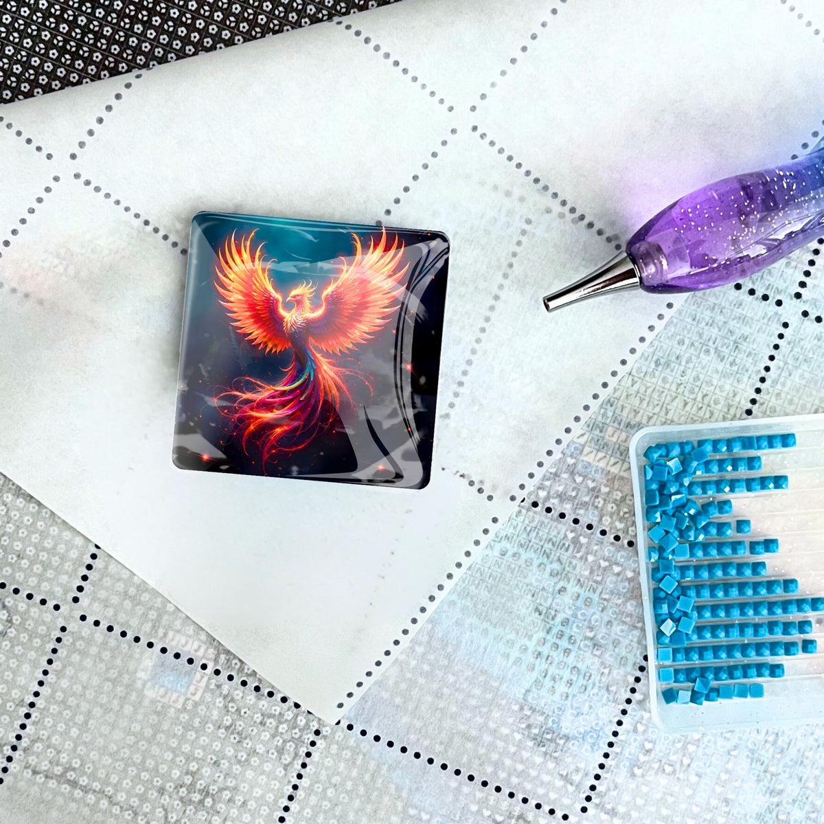 Phönix Cover Minder aus Glas als magnetisches Zubehör für Diamond Painting auf einer Leinwand mit Stift und Steinchen.
