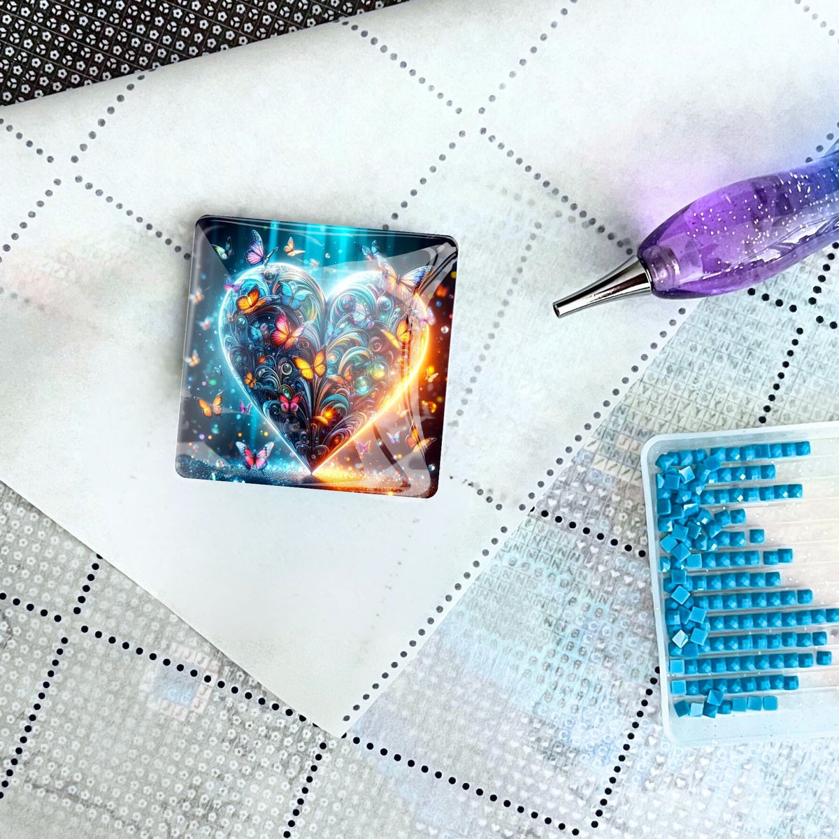 Glas-Cover Minder mit Schmetterlingsherz-Motiv auf einer Diamond Painting Leinwand mit Stift und Steinchen.