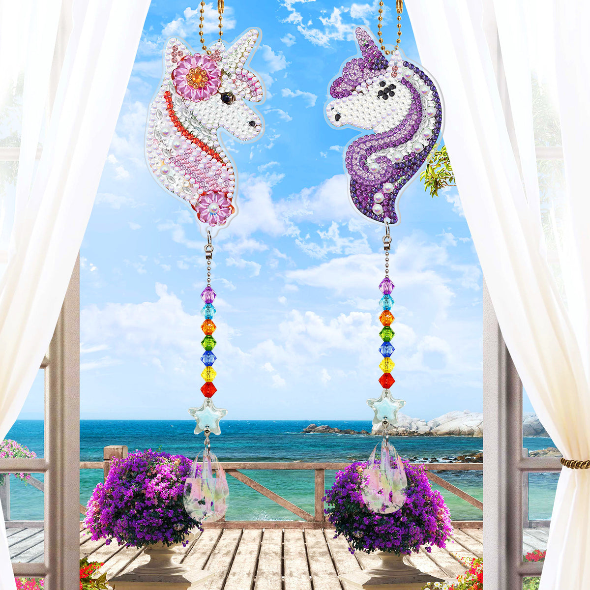 Zwei glitzernde Einhorn Diamond Painting Aufhänger mit bunten Schmucksteinen vor einem traumhaften Meerblick-Fenster.
